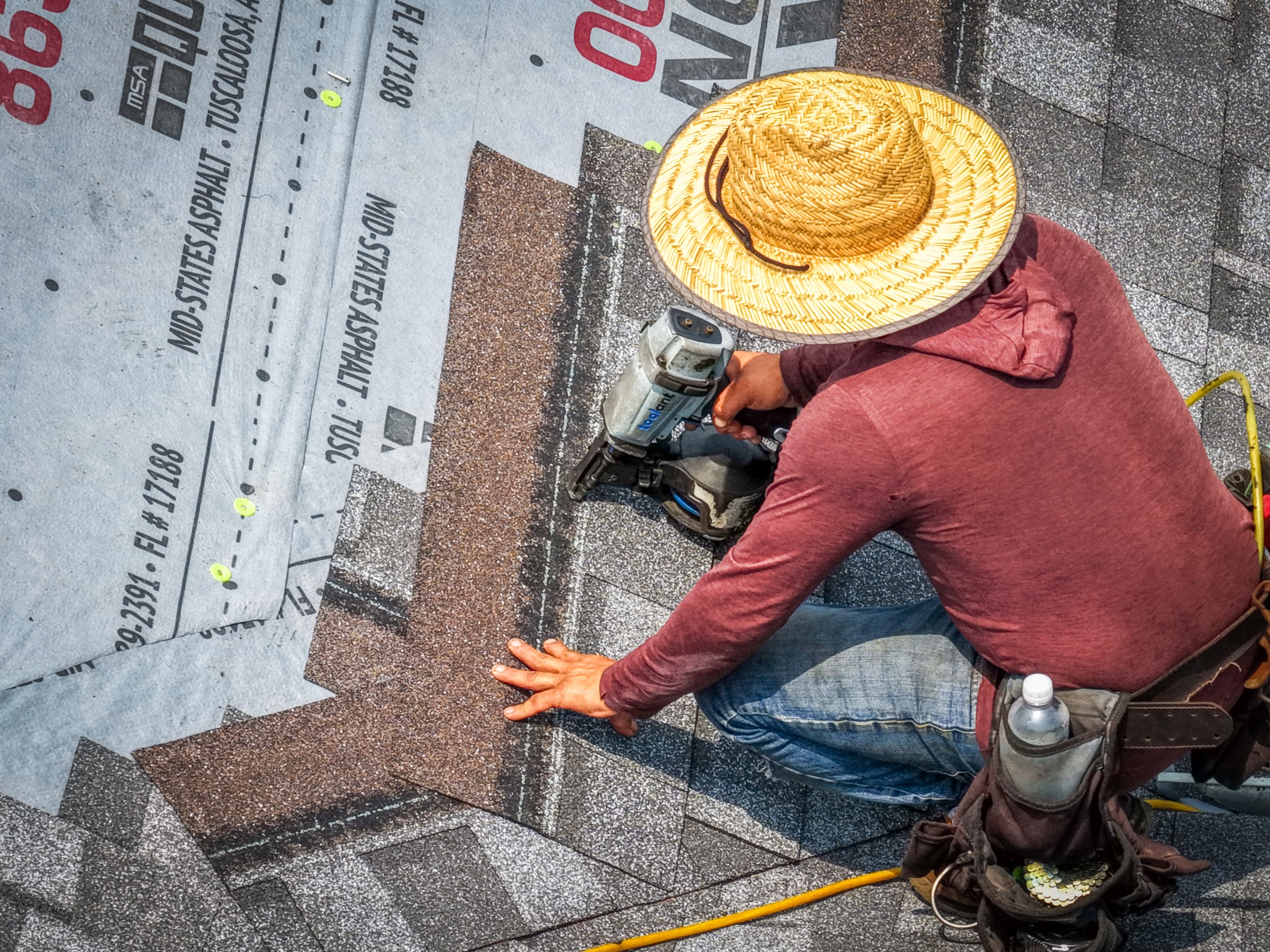 Brogdon roofer in a straw hat carefully fastening architectural shingles